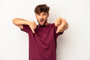 Gri arka planda izole edilmiş genç melez adam baş parmağını aşağı gösteriyor ve hoşlanmadığını ifade ediyor..