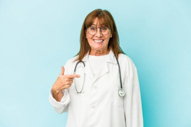 Middle age doctor woman isolated on pink background person pointing by hand to a shirt copy space, proud and confident