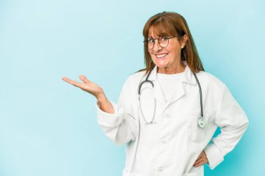 Middle age doctor woman isolated on pink background showing a copy space on a palm and holding another hand on waist.