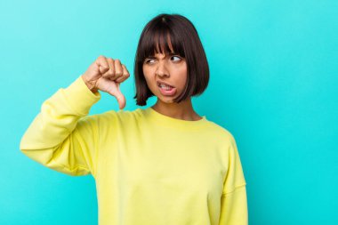 Mavi arka planda izole edilmiş genç bir ırk kadını baş parmağını aşağı gösteriyor ve hoşlanmadığını ifade ediyor..