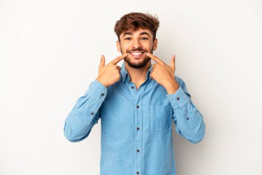 Genç melez adam gri arka planda izole edilmiş gülümsüyor, parmaklarını ağıza doğrultuyor..