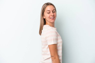 Mavi arka planda soyutlanmış genç beyaz kadın gülümseyen, neşeli ve keyifli bir tarafa bakıyor..