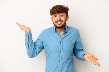 Genç melez adam, gri arka planda izole edilmiş. Kopya alanını tutmak için kafası karışmış ve omuz silkiyor..