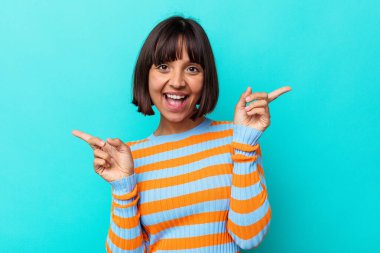 Mavi arka planda izole edilmiş genç bir ırk kadını farklı kopya alanlarını gösteriyor, birini seçiyor, parmaklarıyla gösteriyor.