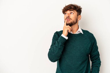 Genç melez adam gri arka planda izole edilmiş şüpheli ve şüpheci bir ifadeyle yana bakıyor..