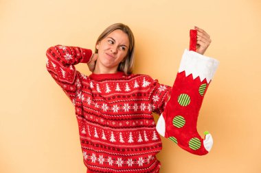 Kafkasyalı genç bir kadın sarı arka planda izole edilmiş bir elf çorabı tutuyor kafasının arkasına dokunuyor, düşünüyor ve bir seçim yapıyor..