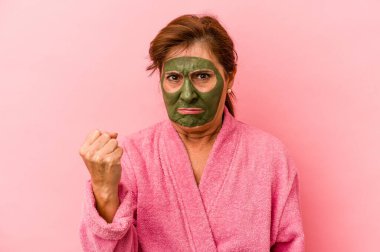 Middle age caucasian woman wearing a facial mask isolated on pink background showing fist to camera, aggressive facial expression.