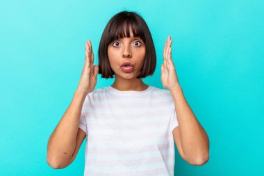 Genç melez kadın mavi arka planda izole edilmiş şaşırmış ve şok olmuş..