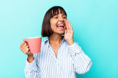 Mavi arka planda izole edilmiş pembe kupa tutan genç bir ırk kadını bağırıyor ve avuç içini açık tutuyor..