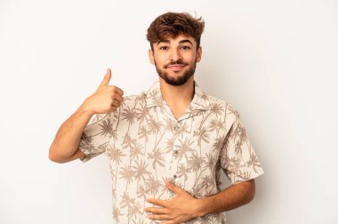 Genç melez adam gri arka planda izole edilmiş karnına dokunuyor, nazikçe gülümsüyor, yemek yiyor ve tatmin oluyor..