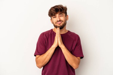 Genç melez adam, gri arka planda izole edilmiş, el ele tutuşmuş, ağzının kenarında dua ediyor, kendinden emin..