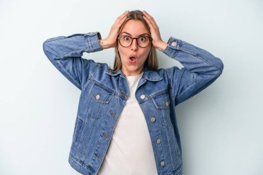 Mavi arka planda izole edilmiş genç beyaz kadın şaşırdı ve şok oldu..