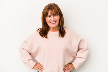 Beyaz arka planda izole edilmiş orta yaşlı beyaz kadın ellerini kalçasında tutuyor..