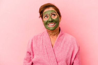 Middle age caucasian woman wearing a facial mask isolated on pink background dreaming of achieving goals and purposes