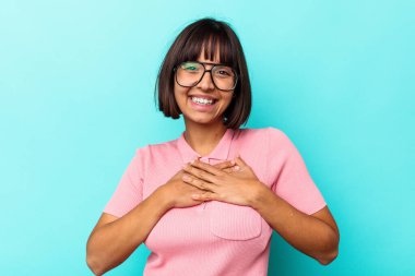 Mavi arka planda izole edilmiş genç melez kadın avuçlarını göğsüne bastıran dostane bir ifadeye sahip. Aşk konsepti.