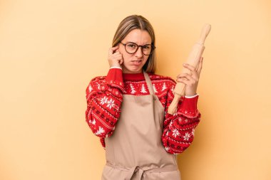 Genç fırıncı kadın Noel için kurabiye yapıyor sarı arka planda izole edilmiş kulakları elleriyle kapatıyor..