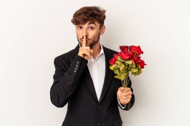 Genç melez adam elinde gül buketi tutuyor beyaz arka planda izole edilmiş bir şekilde ya sır saklıyor ya da sessizlik istiyor..