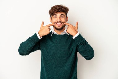 Genç melez adam gri arka planda izole edilmiş gülümsüyor, parmaklarını ağıza doğrultuyor..