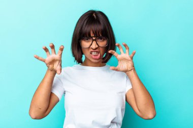 Mavi arka planda izole edilmiş genç melez kadın pençelerini kedi taklidi yaparken gösteriyor, agresif bir hareket..