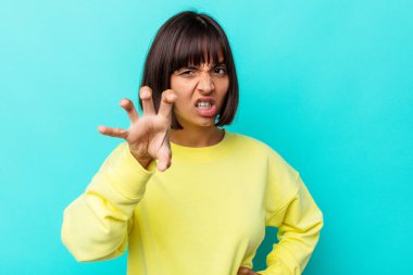 Mavi arka planda izole edilmiş genç melez kadın pençelerini kedi taklidi yaparken gösteriyor, agresif bir hareket..