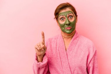 Middle age caucasian woman wearing a facial mask isolated on pink background showing number one with finger.