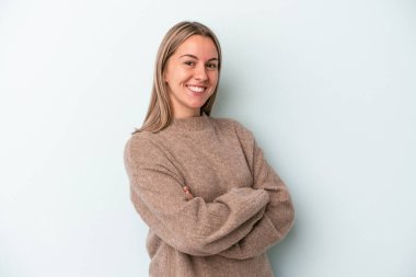 Mavi arka planda izole edilmiş genç beyaz kadın kendini güvende hissediyor, kararlılıkla kollarını kavuşturuyor..