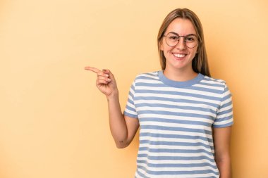 Sarı arka planda izole edilmiş genç beyaz kadın işaret parmağıyla işaret ederek gülümsüyor..