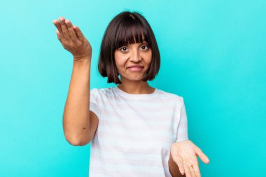 Mavi arka planda soyutlanmış genç melez kadın kollarıyla ölçeği yapıyor, mutlu ve kendinden emin hissediyor..