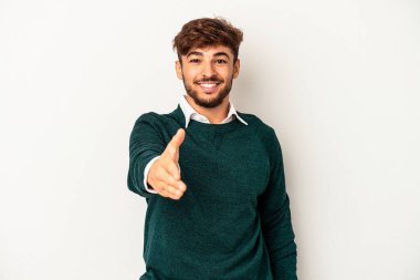 Genç melez adam gri arka planda izole edilmiş kameraya elini uzatarak selam veriyor..