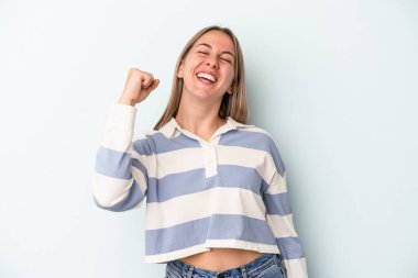 Mavi arka planda izole edilmiş genç beyaz kadın zaferi, tutkuyu ve coşkuyu kutluyor, mutlu bir ifade..