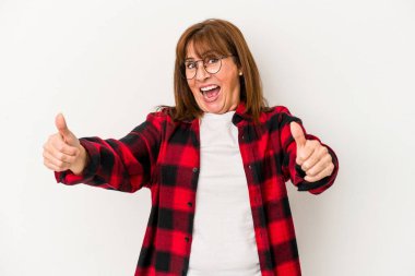 Beyaz arka planda soyutlanmış orta yaşlı beyaz bir kadın. Baş parmağını kaldırıyor, gülümsüyor ve kendinden emin..