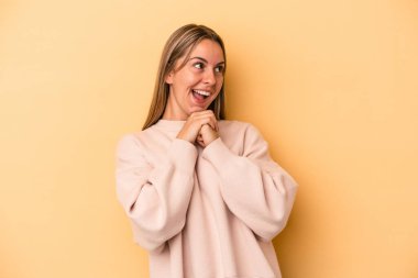 Beyaz tenli genç bir kadın sarı arka planda izole edilmiş şans diliyor, şaşırmış ve ağzını açıp önüne bakıyor..