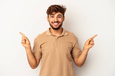 Genç melez adam gri arka planda izole edilmiş farklı kopya alanlarını gösteriyor, birini seçiyor, parmaklarıyla gösteriyor..