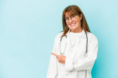 Middle age doctor woman isolated on pink background smiling and pointing aside, showing something at blank space.