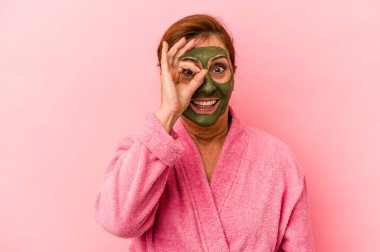 Middle age caucasian woman wearing a facial mask isolated on pink background excited keeping ok gesture on eye.