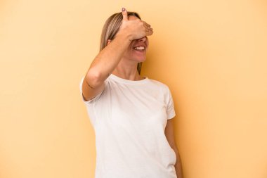 Sarı arka planda izole edilmiş genç beyaz kadın elleriyle gözlerini kapatıyor, geniş bir gülümsemeyle bir sürpriz bekliyor..