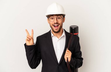 Kask takan genç mimar gri arka planda izole edilmiş neşeli ve kaygısız parmaklarıyla barış sembolü gösteriyor..