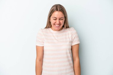 Mavi arka planda izole edilmiş genç beyaz kadın gülüyor ve gözlerini kapıyor, rahatlamış ve mutlu hissediyor..