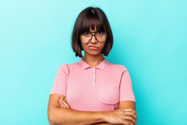 Mavi arka planda soyutlanmış genç melez bir kadın hoşnutsuzca kaşlarını çatmış, kollarını kavuşturmuş..