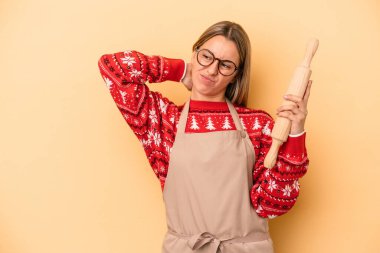 Genç fırıncı kadın Noel için kurabiye yapıyor sarı arka planda izole edilmiş kafasının arkasına dokunuyor, düşünüyor ve bir seçim yapıyor..