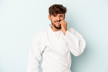 Mavi arka planda karate yapan, tırnak yiyen, gergin ve endişeli genç bir ırk..