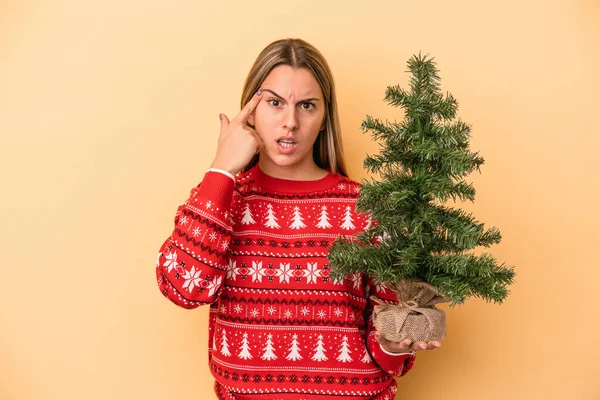 Mladá Běloška Drží Malý Vánoční Stromek Izolované Žlutém Pozadí Ukazuje — Stock fotografie