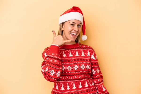 若いですCaucasian女性祝いますクリスマスは指で携帯電話の呼び出しジェスチャーを示す黄色の背景に隔離されました — ストック写真