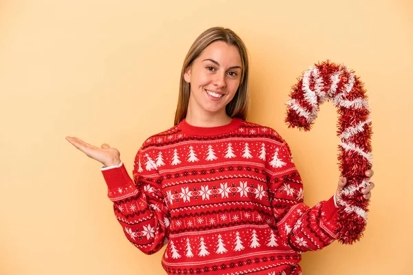 Sarı arka planda izole edilmiş büyük bir noel sopası tutan genç beyaz kadın bir avuç içinde fotokopi alanı ve belinde başka bir el tutuyor..