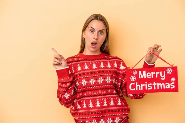 Mladá Běloška Drží Veselé Vánoční Plakát Izolované Žlutém Pozadí Ukazuje — Stock fotografie