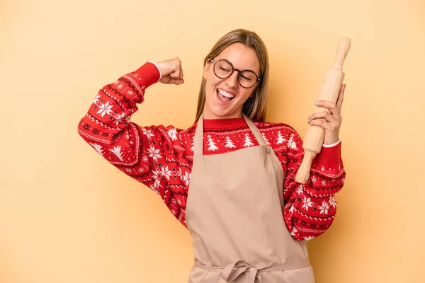 Genç fırıncı kadın Noel için kurabiye yapıyor sarı arka planda izole edilmiş zafer kazandıktan sonra yumruk kaldırıyor, kazanan konsept.