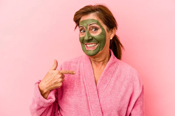 Middle age caucasian woman wearing a facial mask isolated on pink background person pointing by hand to a shirt copy space, proud and confident