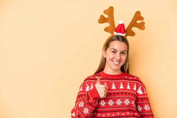 年轻的高加索女人 头戴一顶黄色背景的圣诞驯鹿帽 笑容满面 竖起大拇指 — 图库照片