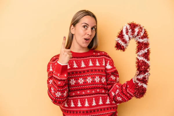 Sarı arka planda izole edilmiş büyük bir noel sopası tutan beyaz bir kadın bir fikri ve ilham konsepti var..
