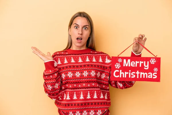Mladá Běloška Drží Veselý Vánoční Plakát Izolované Žlutém Pozadí Překvapené — Stock fotografie